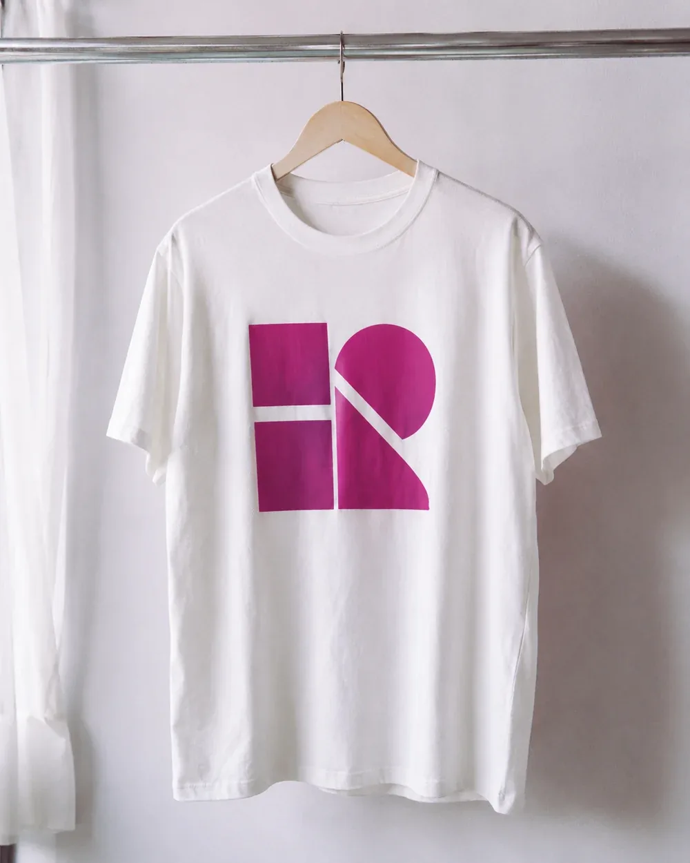 Polo colgado en un gancho de madera, estampado a una tinta magenta en el pecho